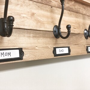 May include: A wooden coat rack with black metal hooks and labels that say "Mom", "Dad", and "Johnny".