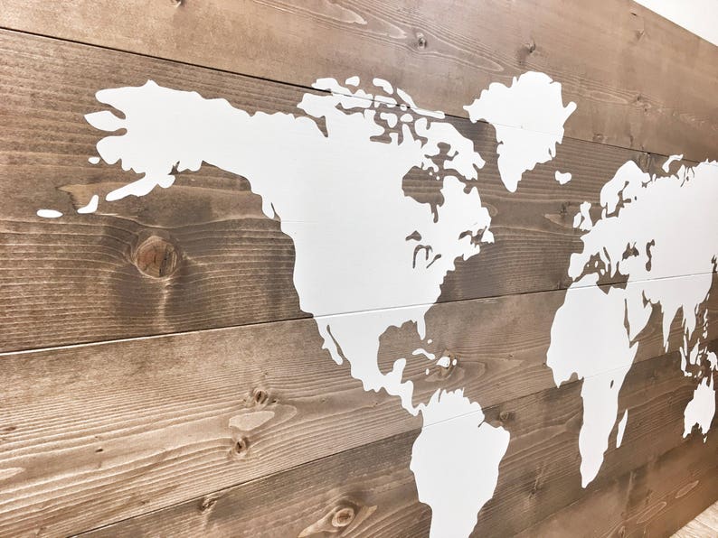 Pode incluir: Um mapa mundial pintado de branco sobre um fundo de madeira marrom. O mapa &eacute; delineado em branco e os continentes s&atilde;o preenchidos com tinta branca.