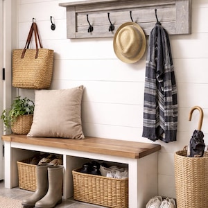 May include: A cozy entryway with a wooden bench, storage baskets, and a wall-mounted coat rack. A woven tote bag, a straw hat, and a striped scarf hang from the hooks. A neutral-toned rug and a potted plant add to the welcoming atmosphere.