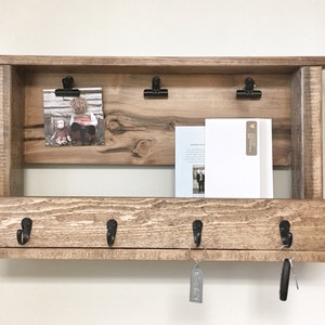 May include: Rustic wooden wall shelf with a top shelf for displaying photos and mail, a lower shelf with three hooks for hanging keys, and a small shelf for storing small items.