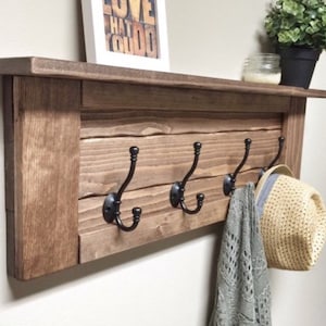 May include: A rustic wooden wall shelf with four black metal hooks. A framed print with the words "DO WHAT YOU LOVE" sits above the hooks. A gray scarf and a straw hat hang from the hooks.