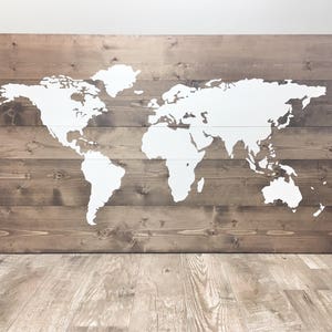 Pode incluir: Um mapa mundial pintado de branco sobre um fundo de madeira marrom. O mapa &eacute; pintado em uma s&eacute;rie de t&aacute;buas de madeira horizontais.