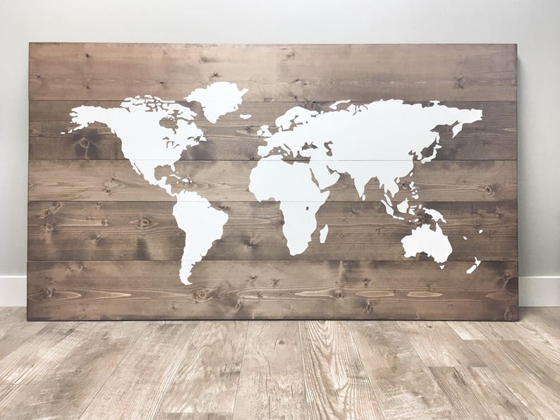 Pode incluir: Um mapa mundial pintado de branco sobre um fundo de madeira marrom. O mapa &eacute; pintado em uma s&eacute;rie de t&aacute;buas de madeira horizontais.