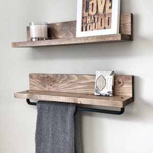 May include: Two rustic wooden floating shelves mounted on a light-colored wall. The top shelf holds a framed print with the words "DO WHAT YOU LOVE WHAT YOU DO". The bottom shelf has a towel bar with a gray towel.