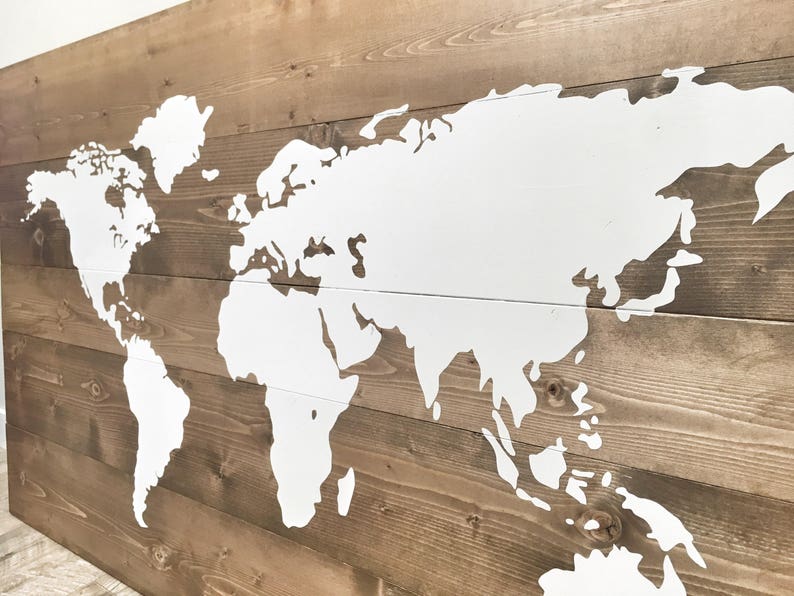 Pode incluir: Um mapa mundial pintado de branco sobre um fundo de madeira marrom. O mapa &eacute; delineado em branco e os continentes s&atilde;o preenchidos com tinta branca.