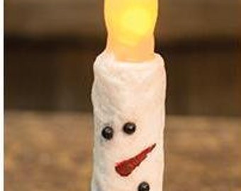 May include: A snowman-themed LED candle with a flickering, warm yellow flame. The white candle has a textured surface and is decorated with black dots for eyes and a red, painted carrot nose. A festive winter decoration.