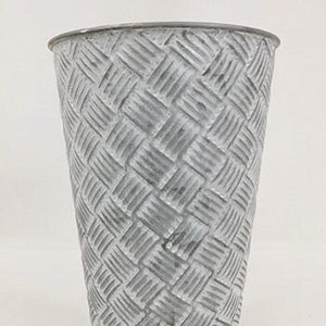 May include: A white metal planter with a woven pattern. The planter is tall and cylindrical.