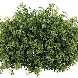 May include: A dense, round, artificial plant with small, rounded green leaves. The plant has a full, lush appearance, with varying shades of green, and is set against a plain white background. The overall shape is compact and symmetrical, suggesting it's a decorative element.