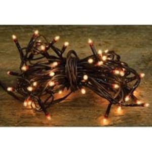 May include: A bundle of warm white string lights with brown wiring, coiled together. The lights are illuminated, casting a soft glow. The lights are on a wooden surface.