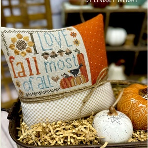 Peut inclure: Un coussin brodé avec le texte "I LOVE FALL MOST OF ALL" par Lindsey Weight. Le coussin est dans un chariot rustique avec des décorations d'automne.