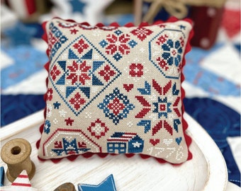May include: A red, white and blue embroidered cushion with a patriotic design. The cushion is on a white wooden tray with red, white and blue stars. The text "PATRIOTIC QUAKER BY LINDSEY WEIGHT" is at the top of the image. The text "PRIMROSE COTTAGE" is at the bottom of the image.