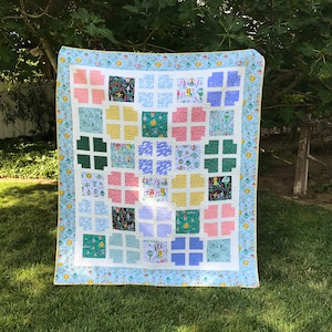 May include: A patchwork quilt with a variety of colorful squares and patterns. The quilt is made with a light blue background and features a yellow, green, pink, and white color scheme.