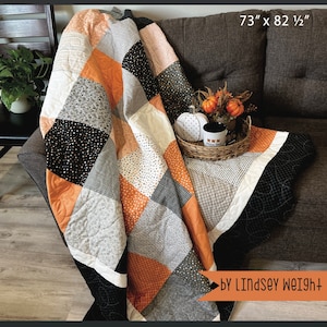 May include: A patchwork quilt in black, white, orange, and grey fabric with a geometric pattern. The quilt is folded and draped over a brown sofa. The quilt measures 73 inches by 82 and a half inches. The text "Piece of cake patchwork" and "Primrose Cottage" are visible in the image.