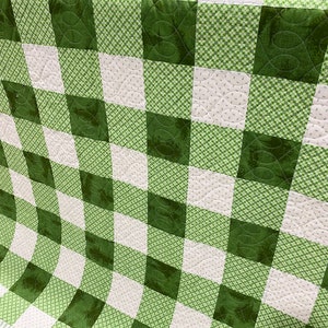 May include: A green and white checkered quilt with a quilted pattern. The quilt is made of fabric with a small floral print.