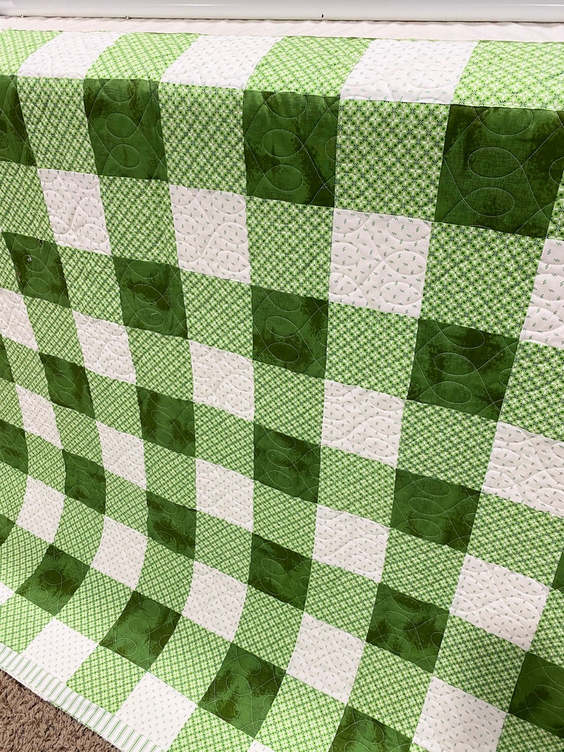 May include: A green and white checkered quilt with a quilted pattern. The quilt is made of fabric with a small floral print.