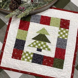 Pode incluir: Um corredor de mesa acolchoado branco com uma borda vermelha e um design de patchwork verde e vermelho com uma árvore de Natal no centro.