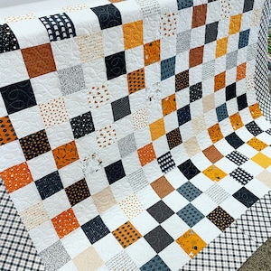Könnte beinhalten: Eine Halloween-Steppdecke mit einem Schachbrettmuster in Schwarz, Weiß, Orange, Braun und Grau. Die Steppdecke besteht aus verschiedenen Stoffen mit unterschiedlichen Mustern, darunter Punkte, Streifen und geometrische Muster.