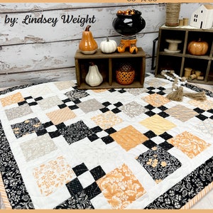 May include: A quilt pattern called "Square it Up" by Lindsey Weight, featuring a black, white, and orange patchwork design. The quilt is 33 inches by 33 inches and is called "Primrose Cottage".