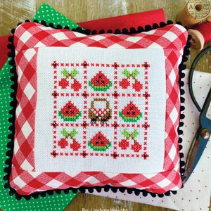 Puede incluir: Una almohada blanca con un borde de cuadros rojos y blancos y pompones negros. La almohada tiene un diseño de punto de cruz de sandías y cerezas. El texto "JUNE nine Patch" está en la parte superior de la imagen. El texto "By: Lindsey Weight" está en la parte inferior de la imagen. El texto "Primrose cottage stitches" está en la parte inferior de la imagen.