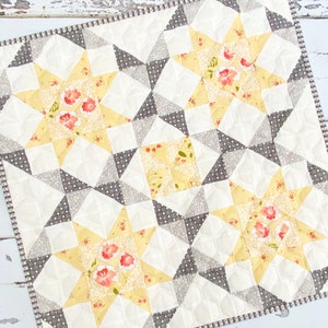 Puede incluir: Una colcha amarilla y gris con un patrón de estrellas. La colcha está hecha de tela con estampado floral. La colcha está acolchada con un patrón de diamante.