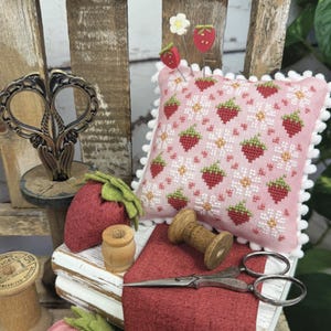 May include: A decorative arrangement with a pink strawberry-patterned pincushion, strawberry pins, and a felt strawberry. The image includes scissors, wooden spools, and the text "STRAWBERRY QUILT" and "PRIMROSE COTTAGE".