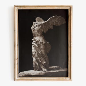 Puede incluir: Impresión en blanco y negro enmarcada de la estatua de la Victoria de Samotracia. La escultura representa una figura alada drapeada, sin cabeza, de pie sobre una base de piedra. El marco es de color dorado claro desgastado.