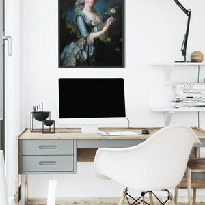 May include: A framed portrait of a woman in a blue and white dress holding a pink rose. The portrait is hanging on a white wall above a desk with a computer, a lamp, and a chair.
