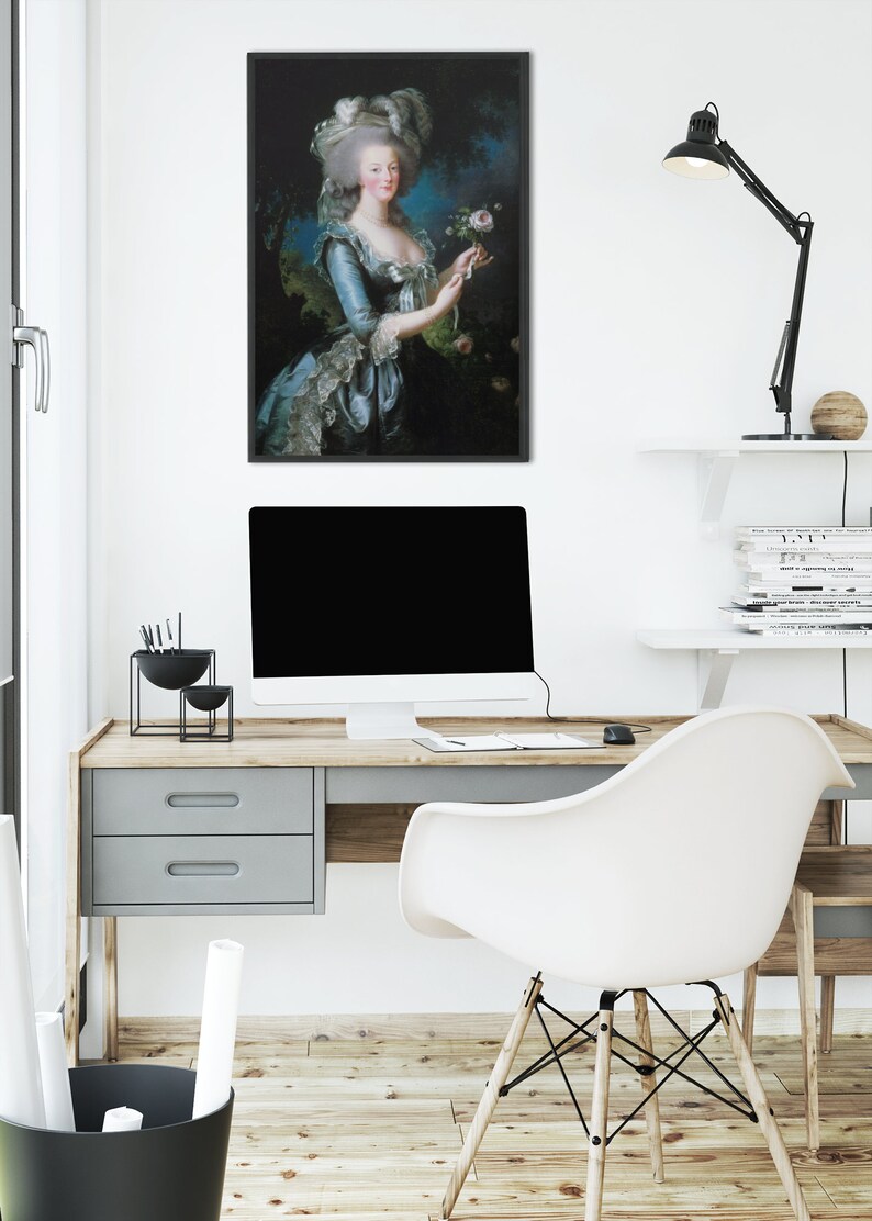 May include: A framed portrait of a woman in a blue and white dress holding a pink rose. The portrait is hanging on a white wall above a desk with a computer, a lamp, and a chair.