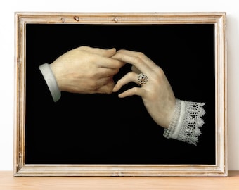 May include: A framed print depicting a Renaissance-style painting of two hands touching. One hand wears a gold ring with a red gemstone. The wrist has a white lace cuff and a string of pearls. The background is black.