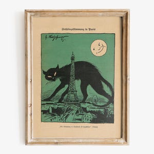 Puede incluir: Impresi&oacute;n vintage enmarcada que presenta un gato negro frente a la Torre Eiffel en Par&iacute;s. La obra de arte tiene una combinaci&oacute;n de colores verde y beige, con una luna sonriente en el cielo. El texto "Fr&uuml;hlingsstimmung in Paris" est&aacute; en la parte superior.