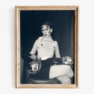 Puede incluir: Fotografía vintage en blanco y negro enmarcada. El sujeto lleva una camiseta de manga larga de color claro con el texto "I AM IN TRAINING DON'T KISS ME". Se ven dos cascos decorativos con texto y diseños. La fotografía está en un marco dorado.