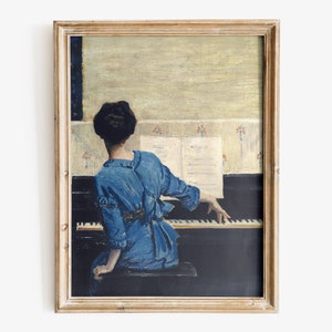 Puede incluir: Una pintura de una persona con un vestido azul tocando un piano. El piano es negro y la persona está sentada en el piano de espaldas al espectador. La pintura está enmarcada en un marco de madera claro.