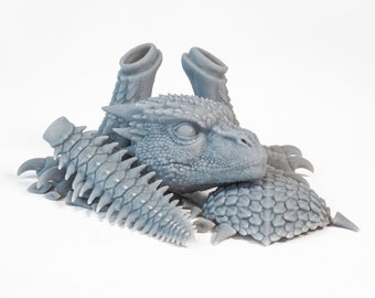 Puede incluir: Modelo de dragón impreso en 3D de color gris con una espalda, cola y garras espinosas. El modelo está en piezas y está listo para ser ensamblado.
