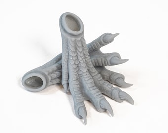 May include: A pair of grey 3D printed dragon feet with claws. The feet are designed to be used as a base for a miniature or other model.