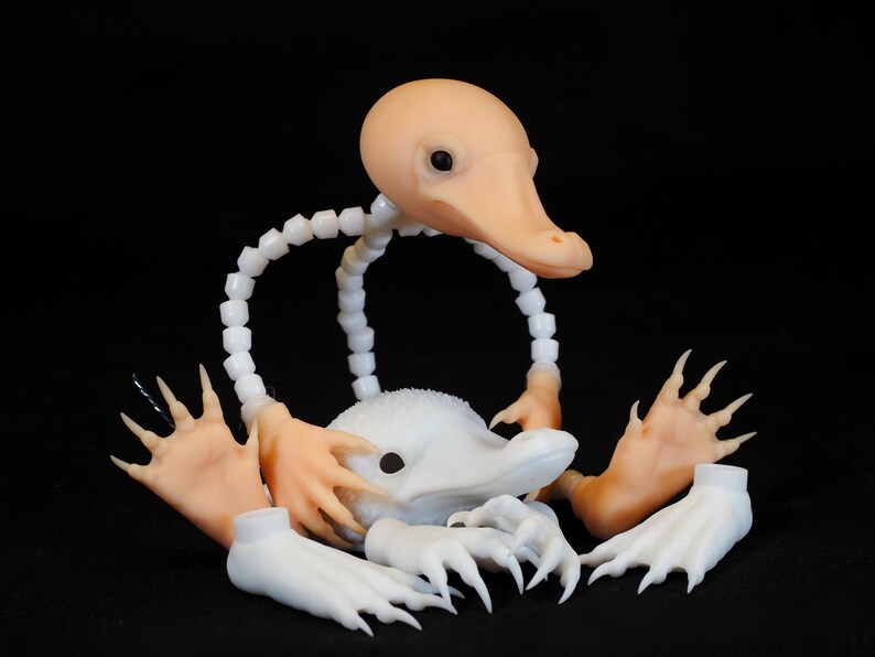 May include: A disassembled, whimsical creature sculpture with a light peach-colored head and beak, white body, and articulated limbs. The sculpture is set against a black background, highlighting its unique design.