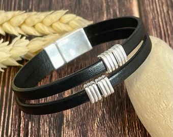 以下が含まれることがあります： 銀色の磁気留め金と銀色の装飾的なアクセントが付いた黒い革のブレスレット