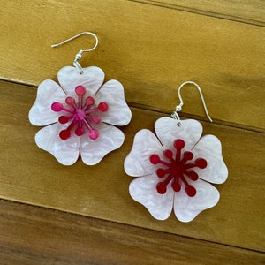 May include: A pair of pink and red flower-shaped earrings with silver hooks. The earrings are made of acrylic and have a marbled effect.