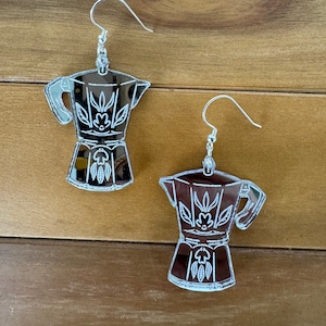 May include: A pair of silver mirrored earrings shaped like a traditional Italian coffee pot with a floral design.