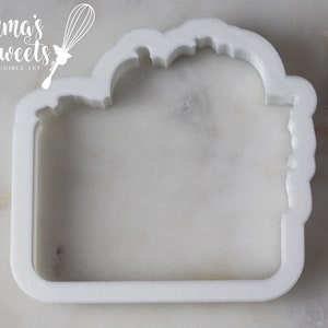 May include: White plastic cookie cutter shaped like a rectangle with a rounded top. The top of the cutter has a decorative design.
