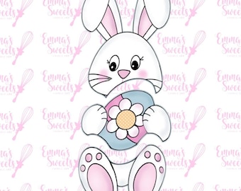 Puede incluir: Un cortador de galletas de conejo blanco sosteniendo un huevo de Pascua azul y rosa con una flor blanca. El conejo tiene orejas y patas rosas.