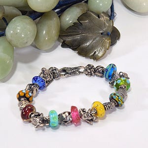 Puede incluir: Una colorida pulsera de cuentas con un cierre y abalorios plateados. La pulsera presenta una variedad de cuentas de vidrio en tonos azules, amarillos, verdes, naranjas y rojos. Los abalorios plateados se intercalan. La pulsera mide unos 18 cm de largo.