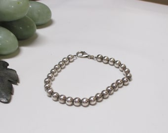 May include: A silver-toned beaded bracelet featuring a continuous strand of polished, spherical metal beads. The bracelet is secured with a small, functional lobster claw clasp mechanism, creating a simple and uniform circular design.