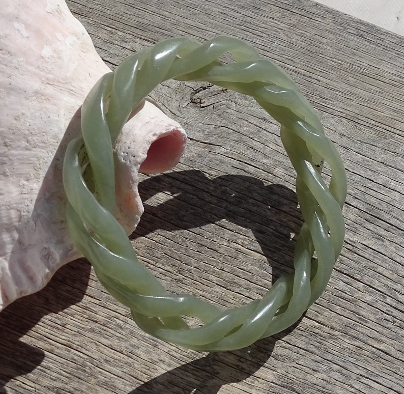 May include: A green jade bangle bracelet with a braided design. The bracelet is made of a smooth, polished jade and has a natural, earthy look.