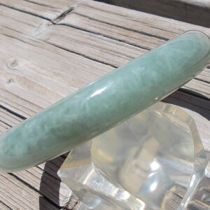 May include: A light green jade bangle bracelet with a swirling pattern. The bracelet is smooth and polished.