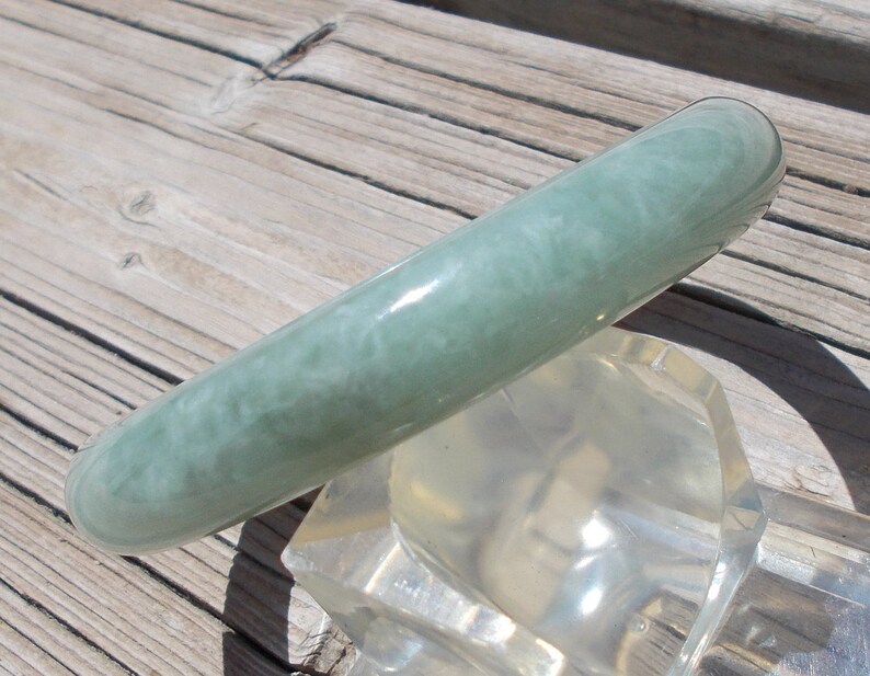 May include: A light green jade bangle bracelet with a swirling pattern. The bracelet is smooth and polished.