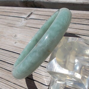 May include: A light green jade bangle bracelet. The bracelet is smooth and polished, with a subtle swirl pattern.