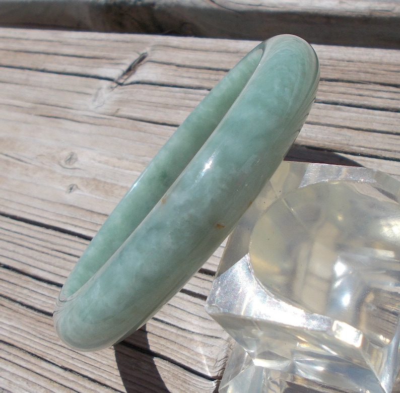 May include: A light green jade bangle bracelet. The bracelet is smooth and polished, with a subtle swirl pattern.