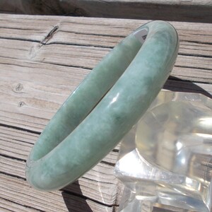 May include: A light green jade bangle bracelet. The bracelet is smooth and polished, with a subtle marbled pattern.