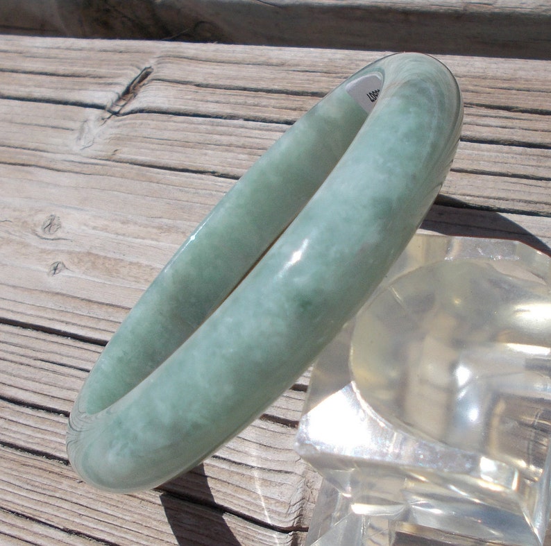 May include: A light green jade bangle bracelet. The bracelet is smooth and polished, with a subtle marbled pattern.