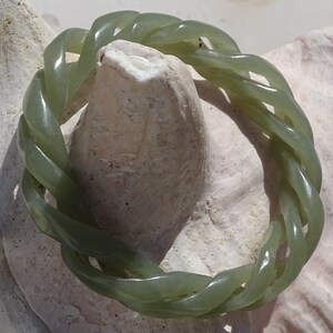 May include: A green jade bracelet with a braided design. The bracelet is made of a smooth, polished jade and has a natural green color.